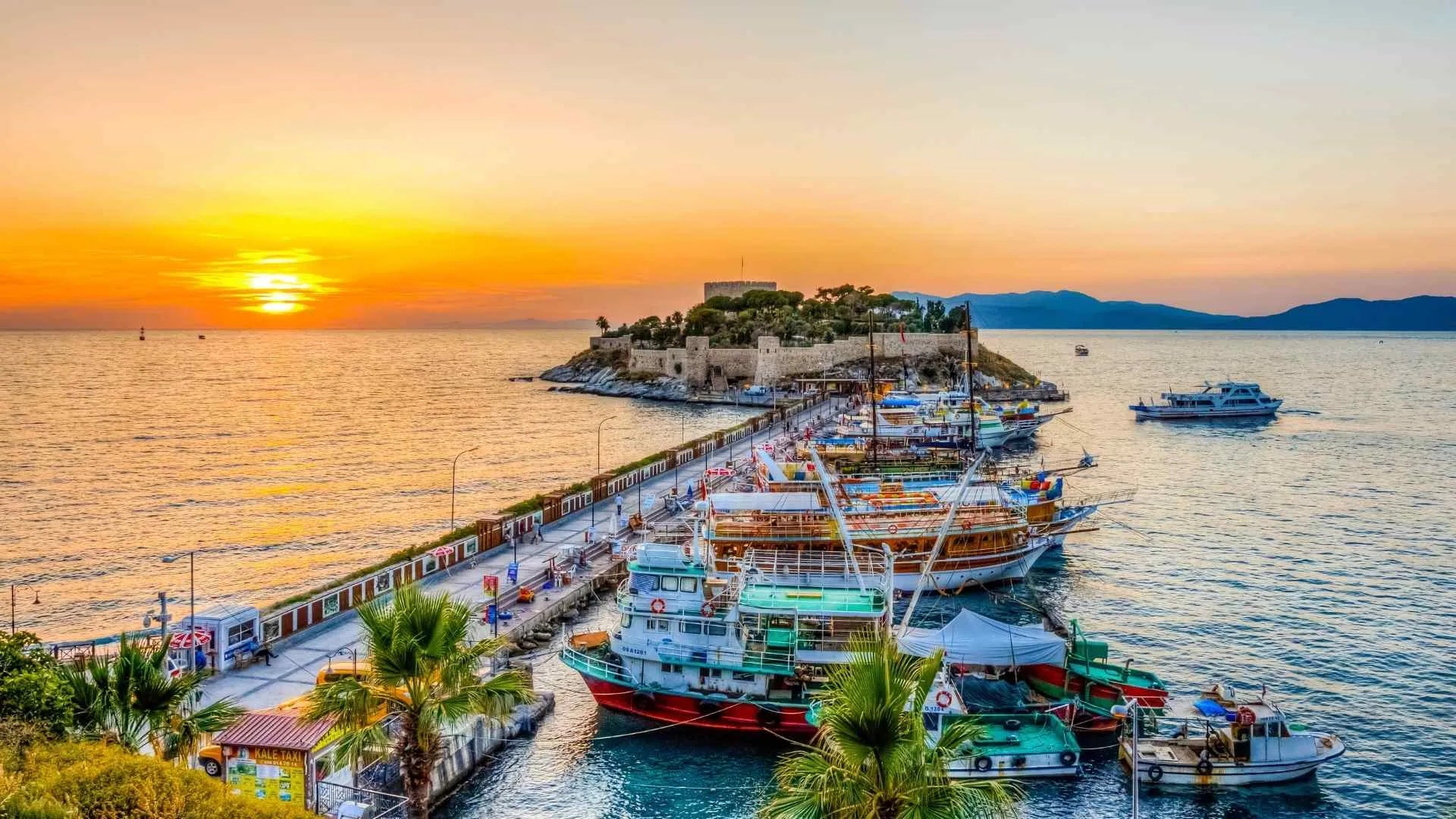 Sunset over a coastal scene with boats docked along a pier in KUSADAI.