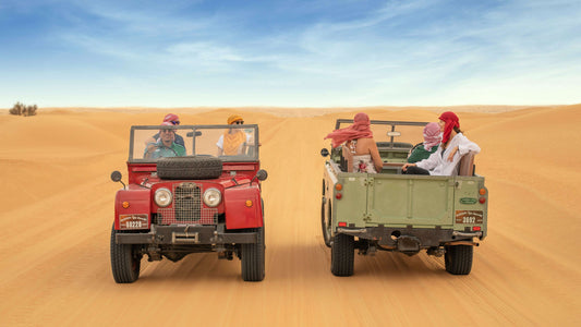 A classic vintage Land Rover driving through the golden sands of the Dubai desert.